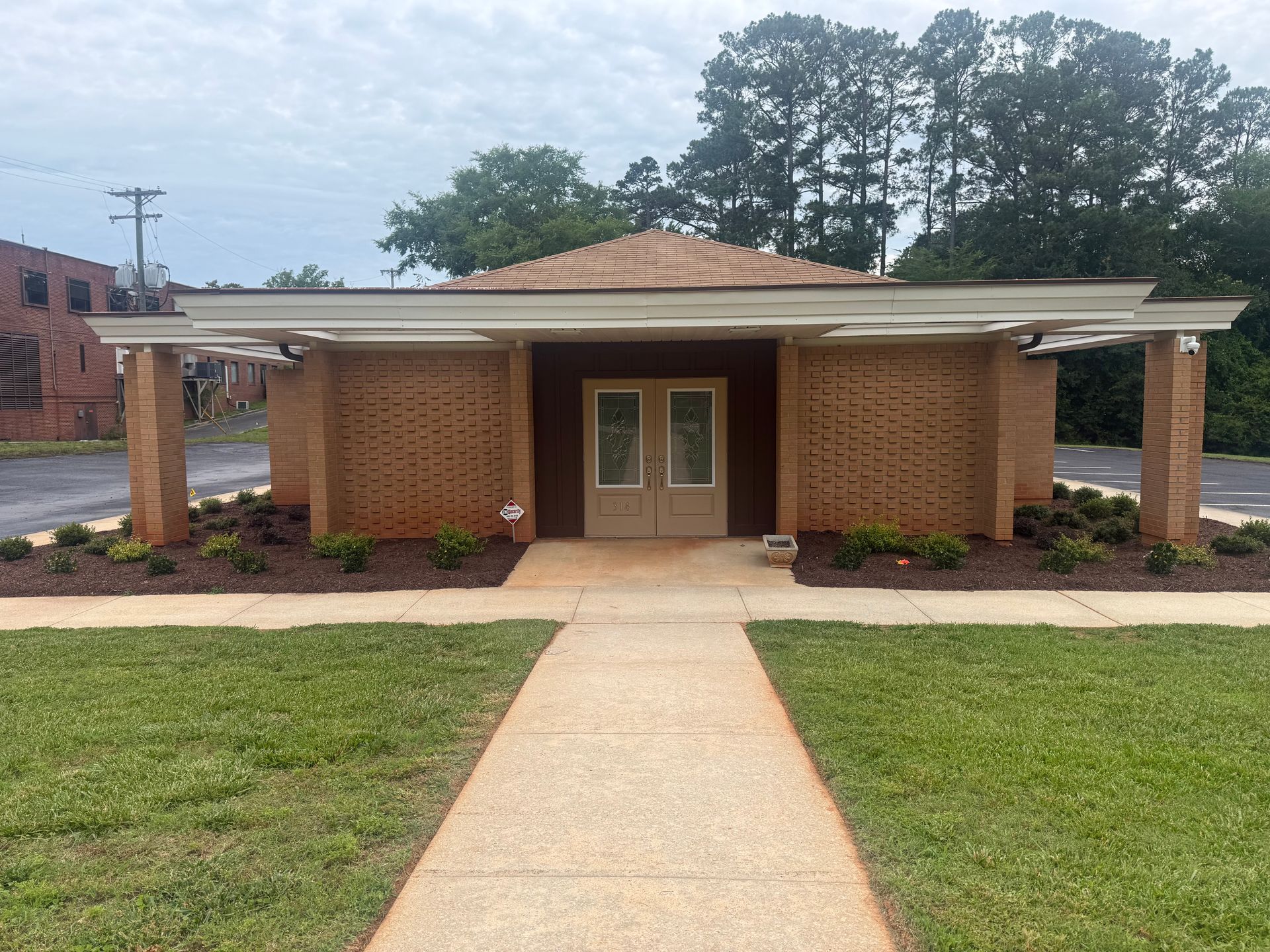 Brick building with double doors and covered entrance, fronted by a concrete walkway and grass lawn
