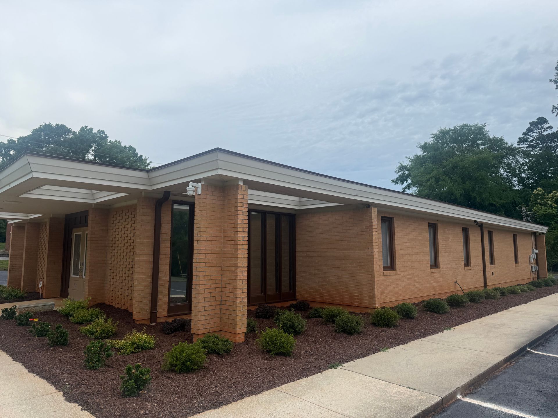 Single-story brick office building with a covered entrance and sidewalk on an overcast day