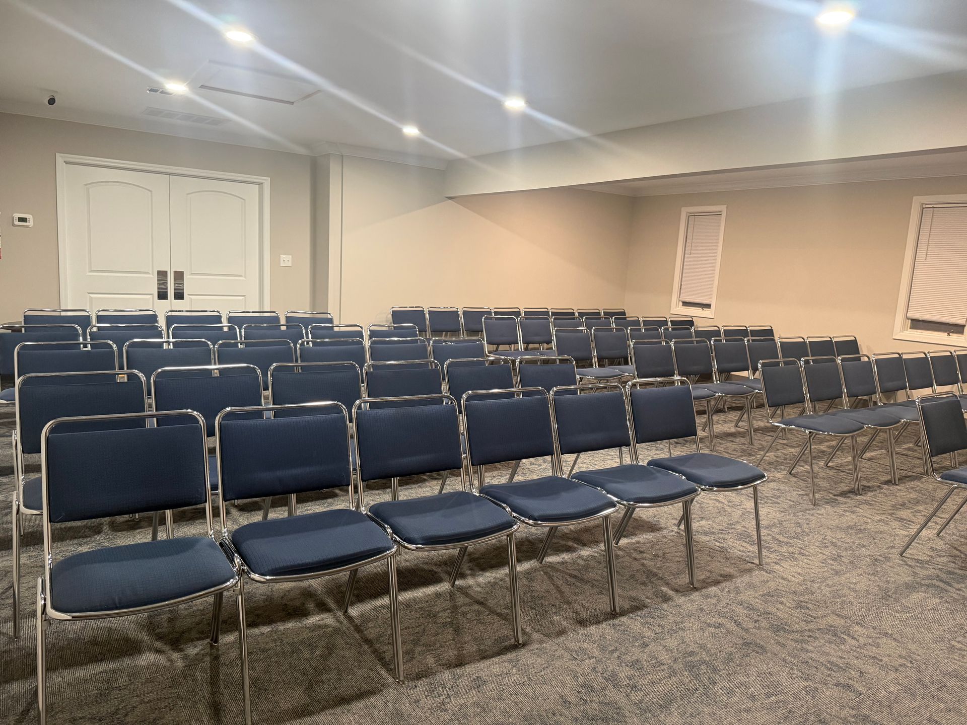 Empty conference room with rows of blue chairs facing the front under recessed ceiling lights.
