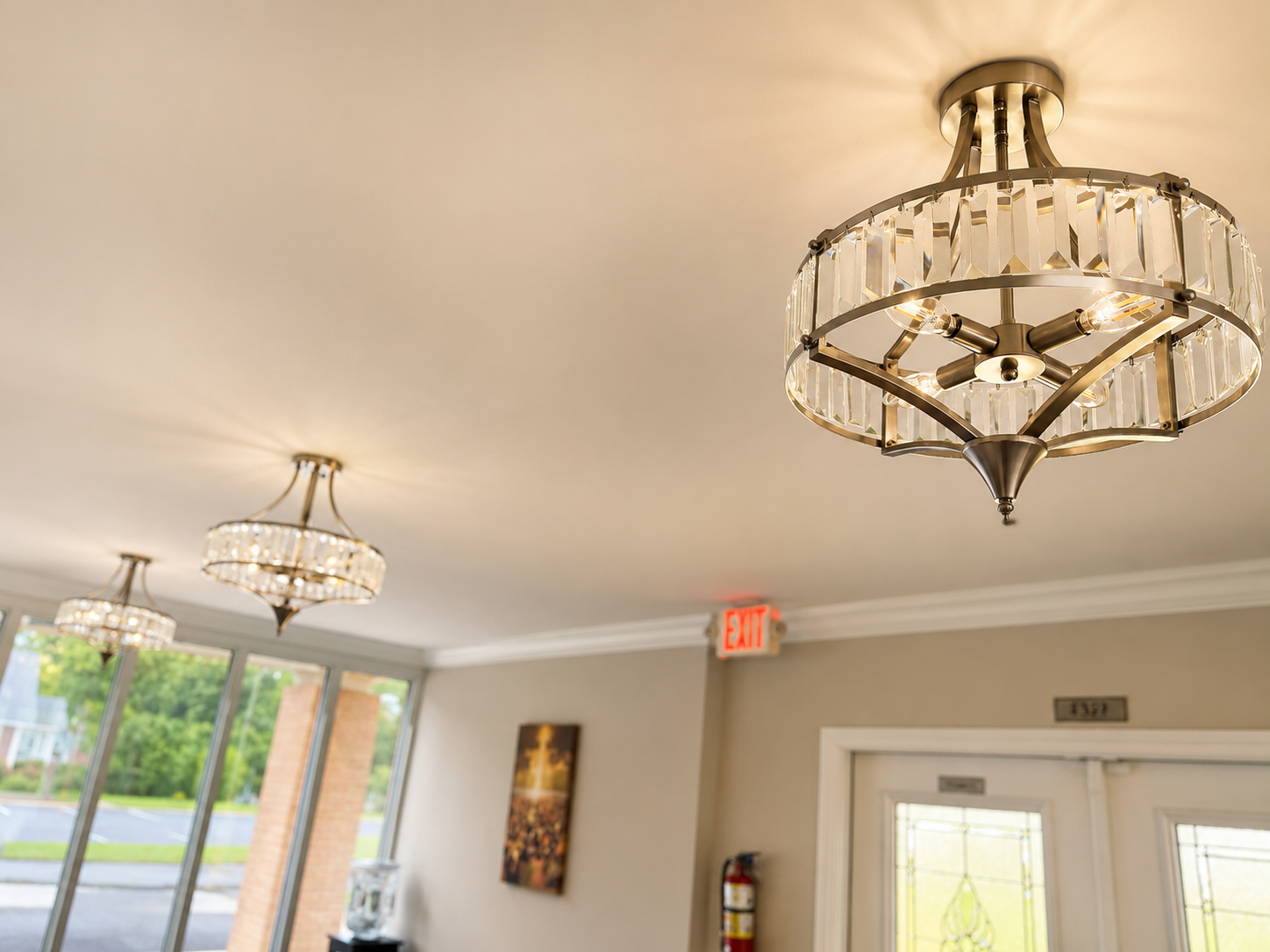 Interior of a lobby with ornate ceiling lights, glass doors, and a wall-mounted fire extinguisher