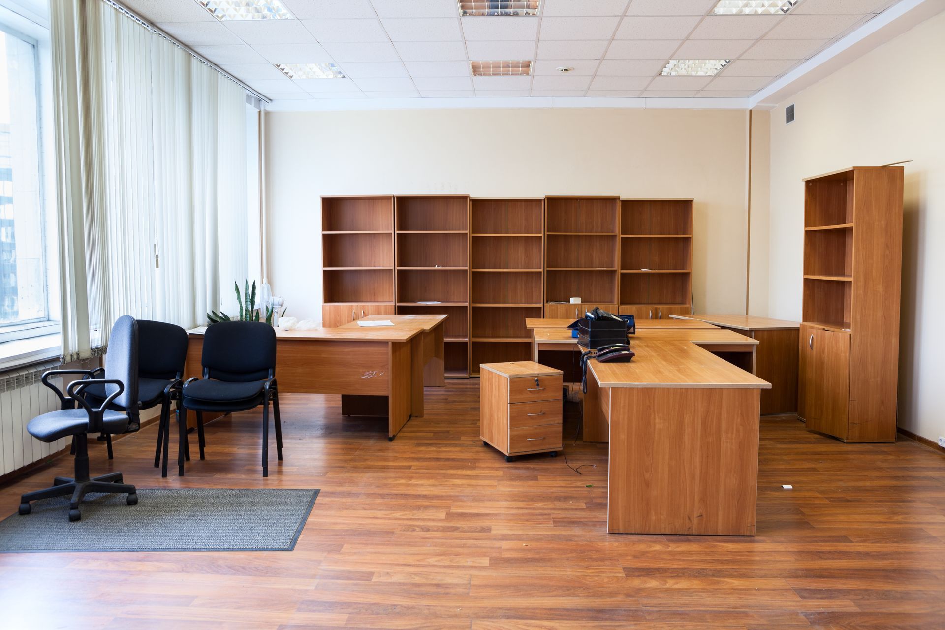 Empty office with wooden desks, shelves, and black chairs on a bright hardwood floor