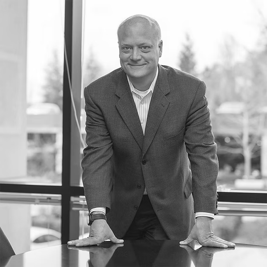 Smiling man in a blazer leaning on a table in a bright office with large windows