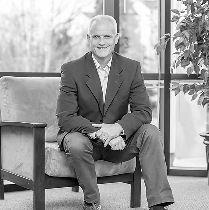 Man sitting on a couch in a bright office lobby, smiling at the camera.