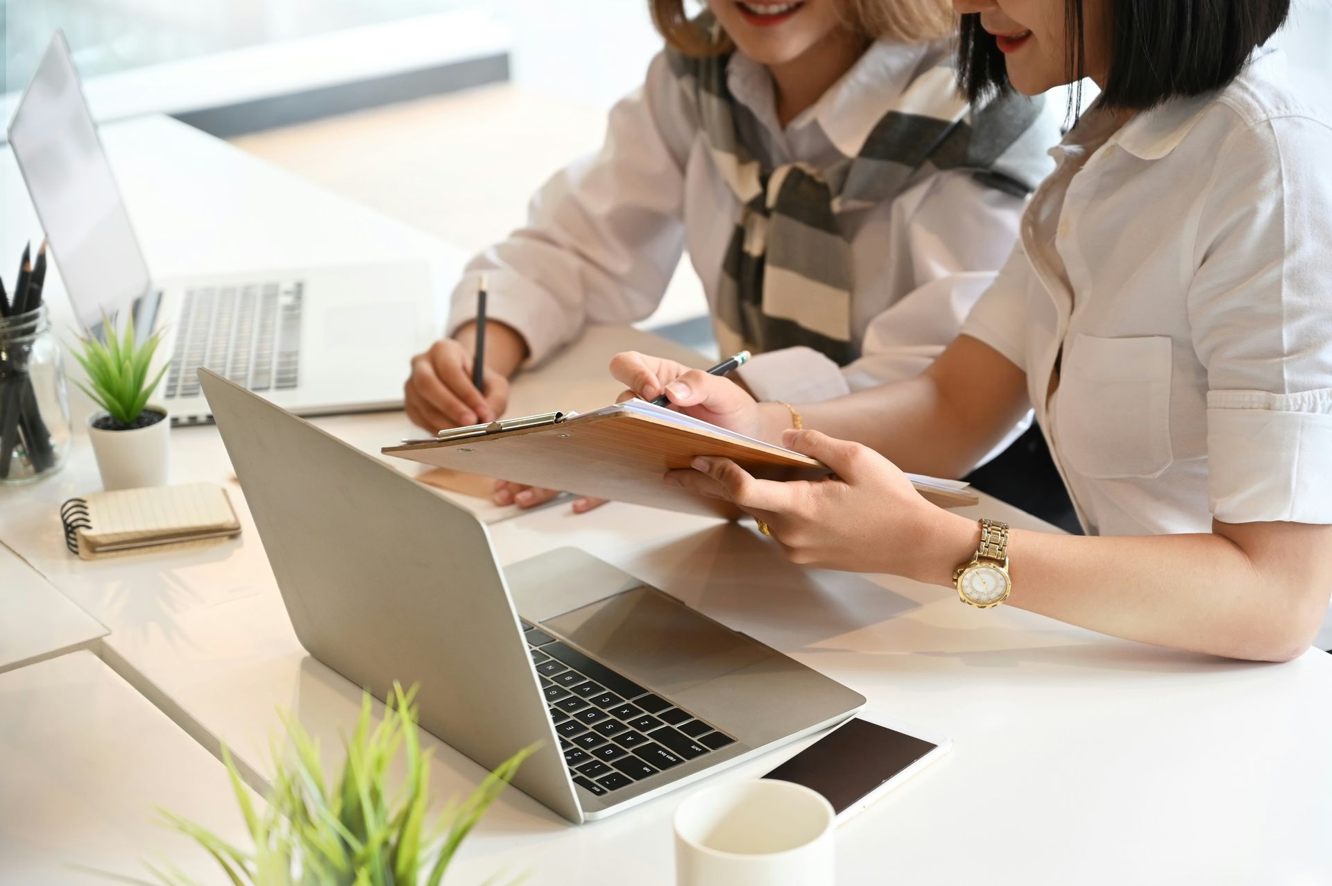 Two coworkers reviewing notes at a laptop in a bright office meeting space