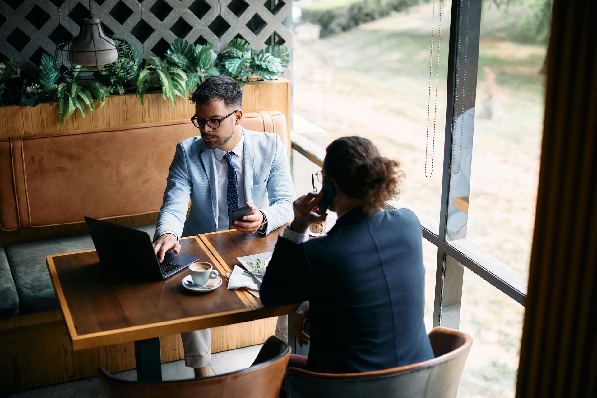 Two people in a cafe sitting at a wooden table, talking over drinks and a phone.