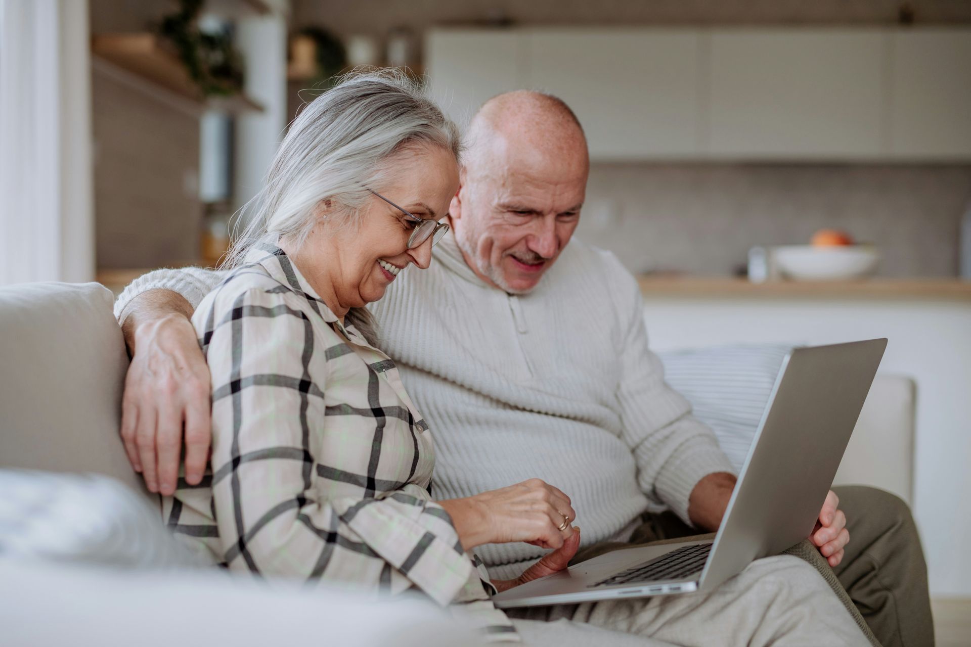 Smiling couple on a couch using a laptop together in a bright living room