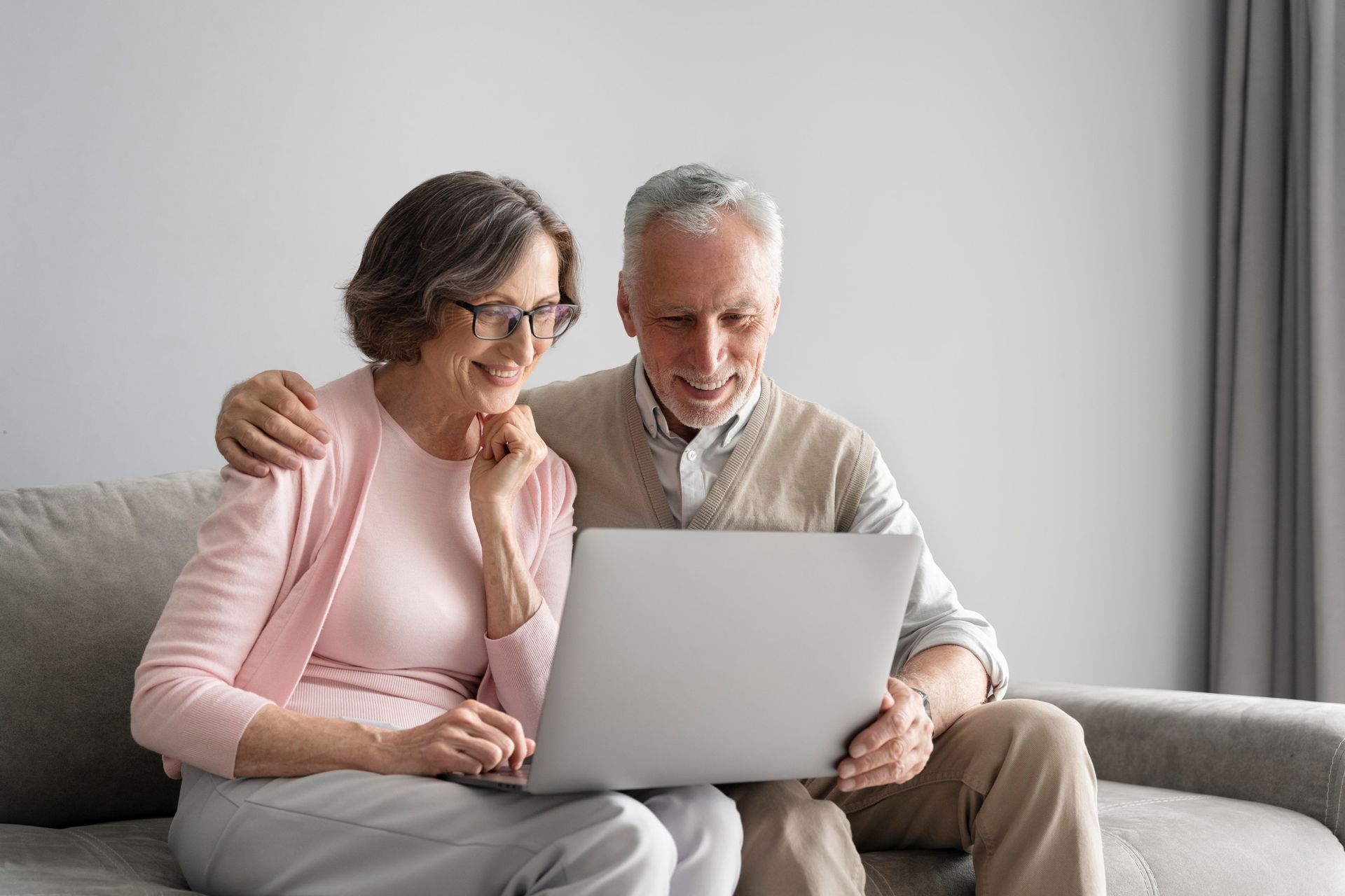 Two people sitting on a couch, smiling and looking at a laptop together.