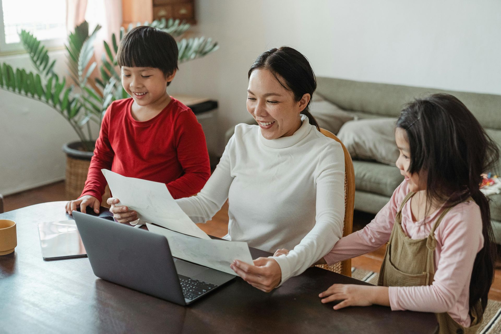 Three people sharing papers and a laptop on a table in a bright living room