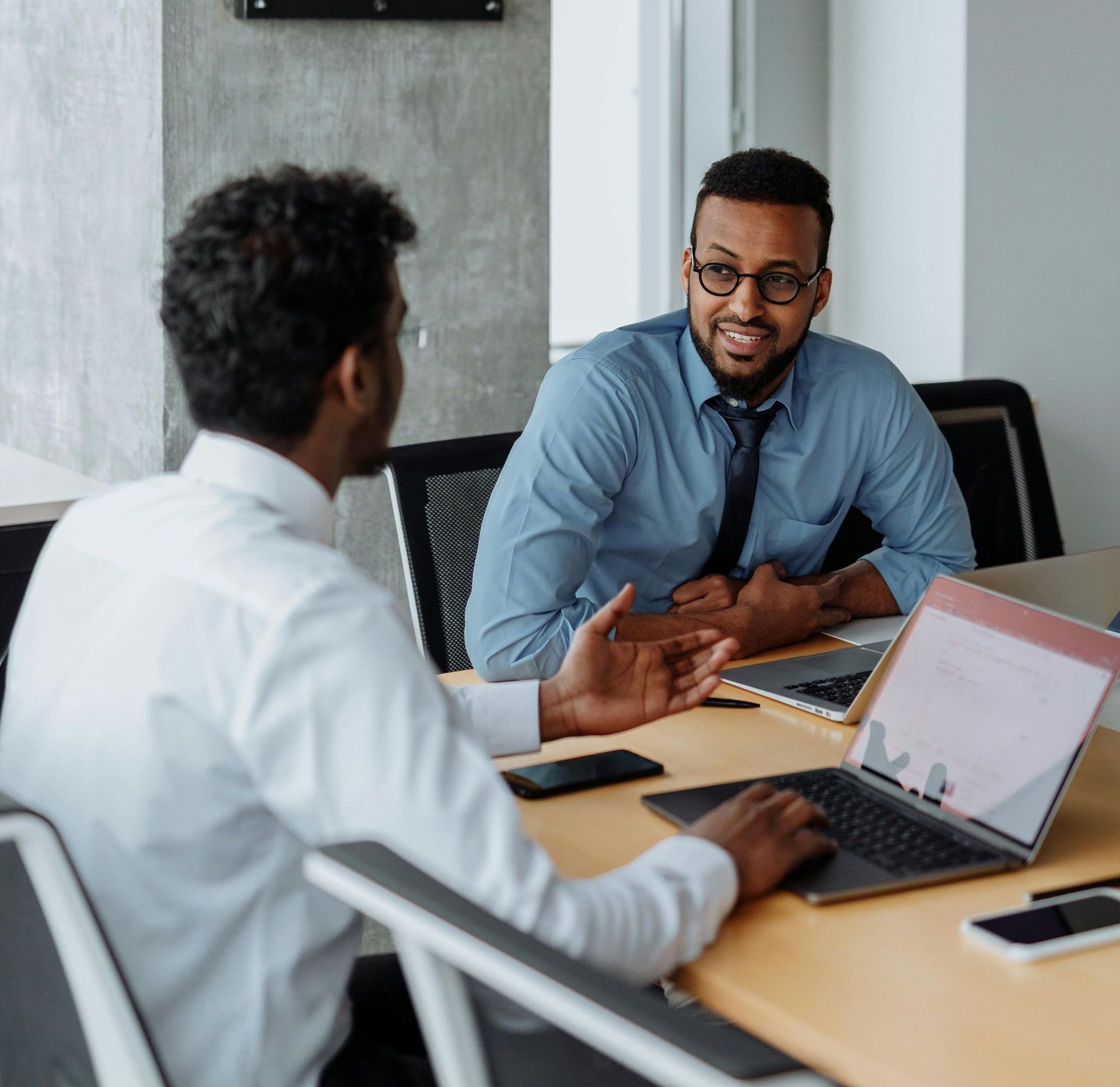 Two coworkers discussing work at a desk with laptops in a modern office