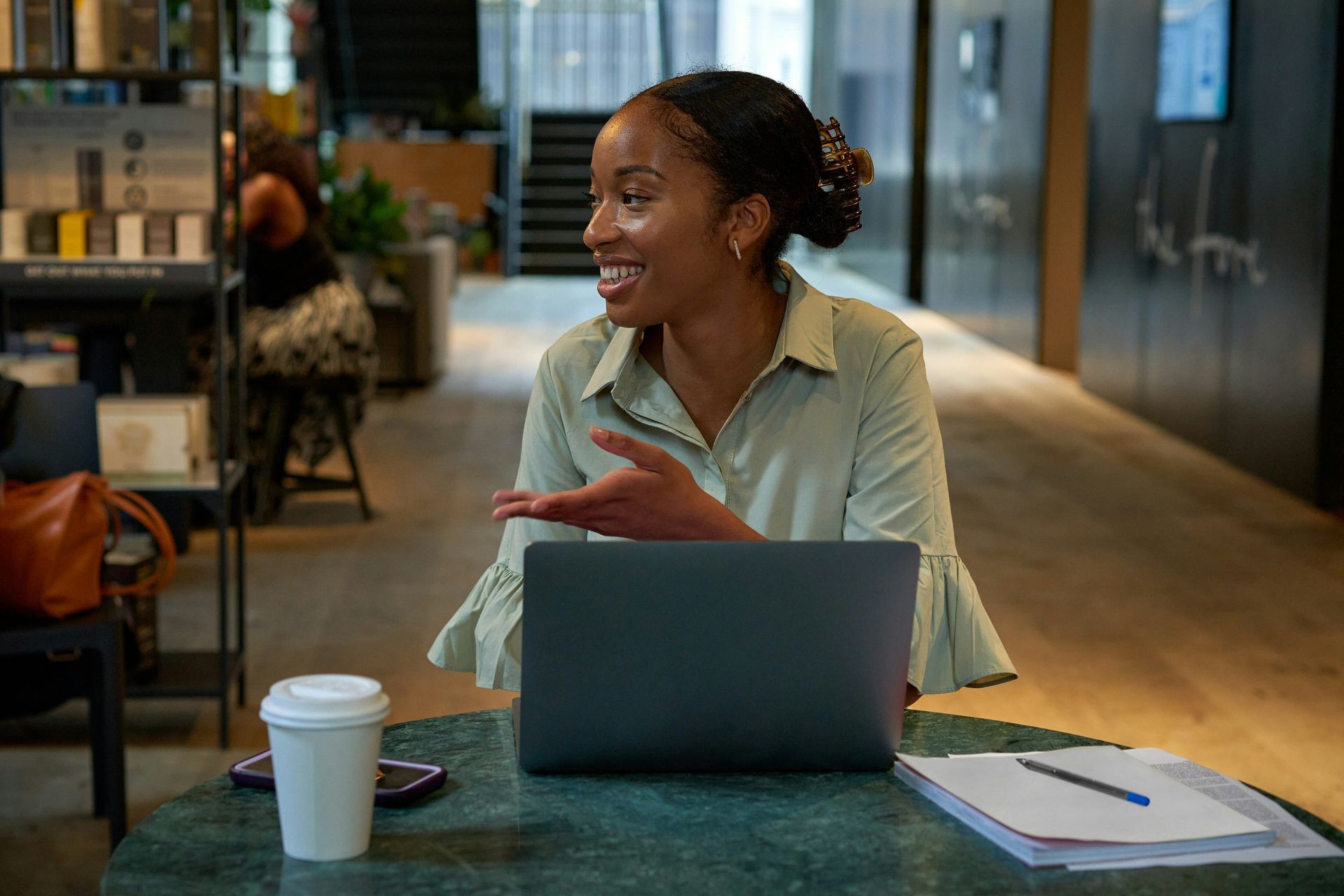 Woman smiling at a laptop in a modern office, with coffee cup and notebook on the table.