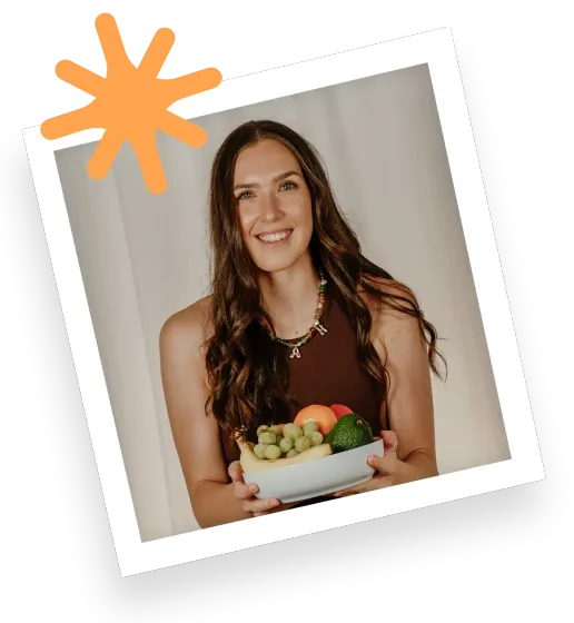 Woman holding a bowl of fresh vegetables and fruit, smiling in a tilted portrait against a light background.