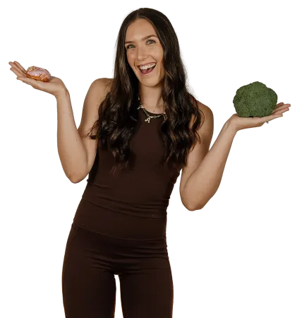 Smiling woman in brown outfit holding a head of broccoli and shrugging on a white background