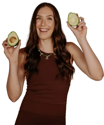Woman smiling and holding two avocado halves against a white background
