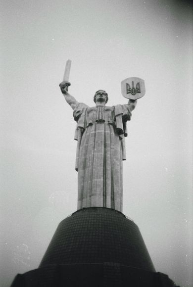 Monumental statue holding a sword and shield atop a domed base against a cloudy sky