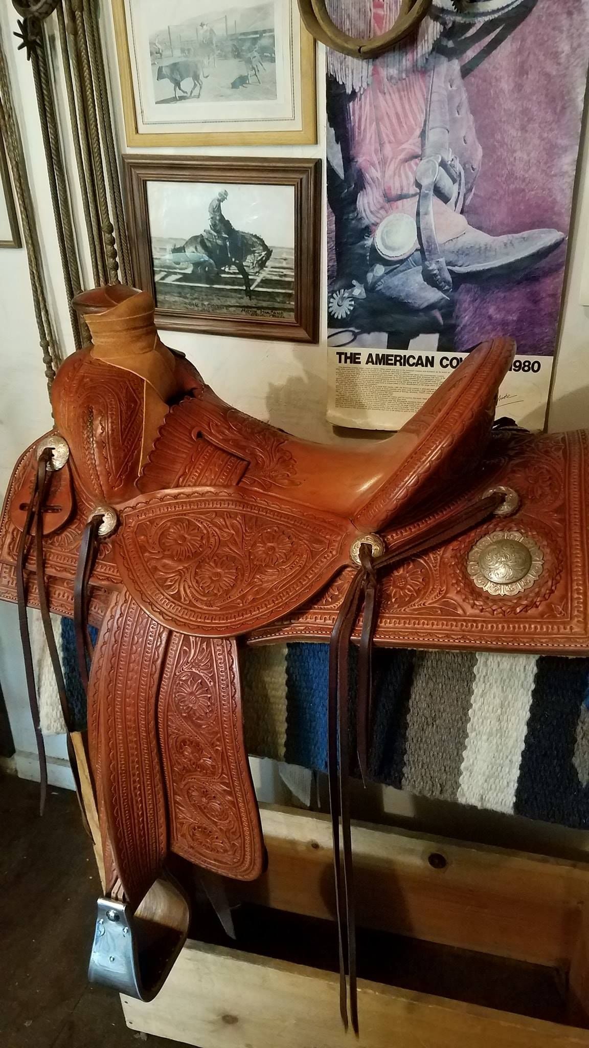 Brown leather saddle on a wooden stand in a room with framed pictures on the wall