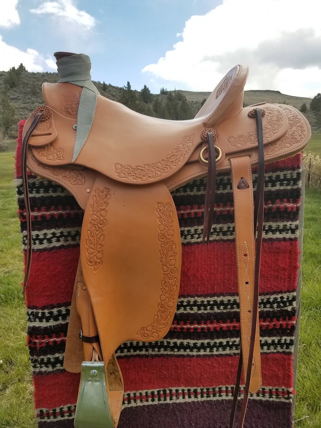 Leather saddle on a patterned blanket, with a matching strap hanging beside it.