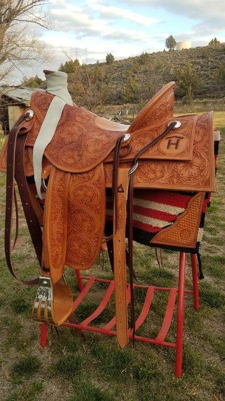 Brown leather saddle on a red stand outdoors, with a blanket and hillside in the background