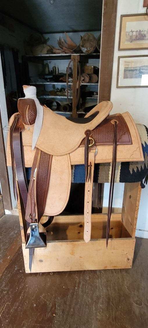 Leather saddle on a wooden display stand in a room, with framed signs on the wall.