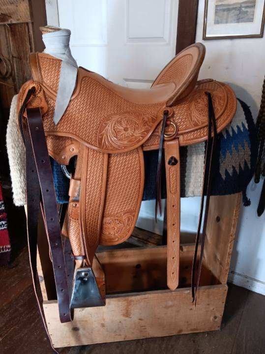 Brown leather western saddle on a wooden stand indoors