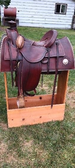 Brown leather saddle on a horse dummy outdoors, with a wooden support frame and white house in background