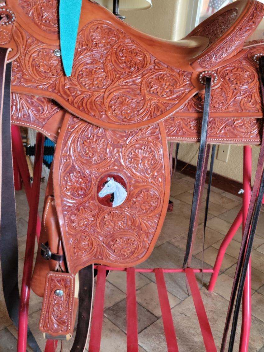 Brown tooled leather saddle with turquoise accents hanging on a stand indoors