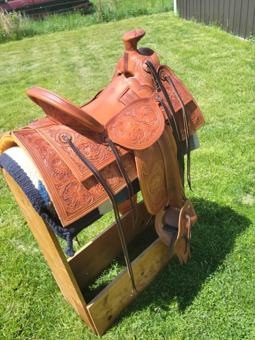 Brown leather saddle on a wooden stand in a sunny grassy yard