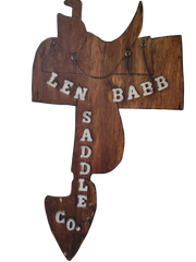 Wooden sign shaped like a fish, painted with &ldquo;LEN BABB SADDLE CO.&rdquo;
