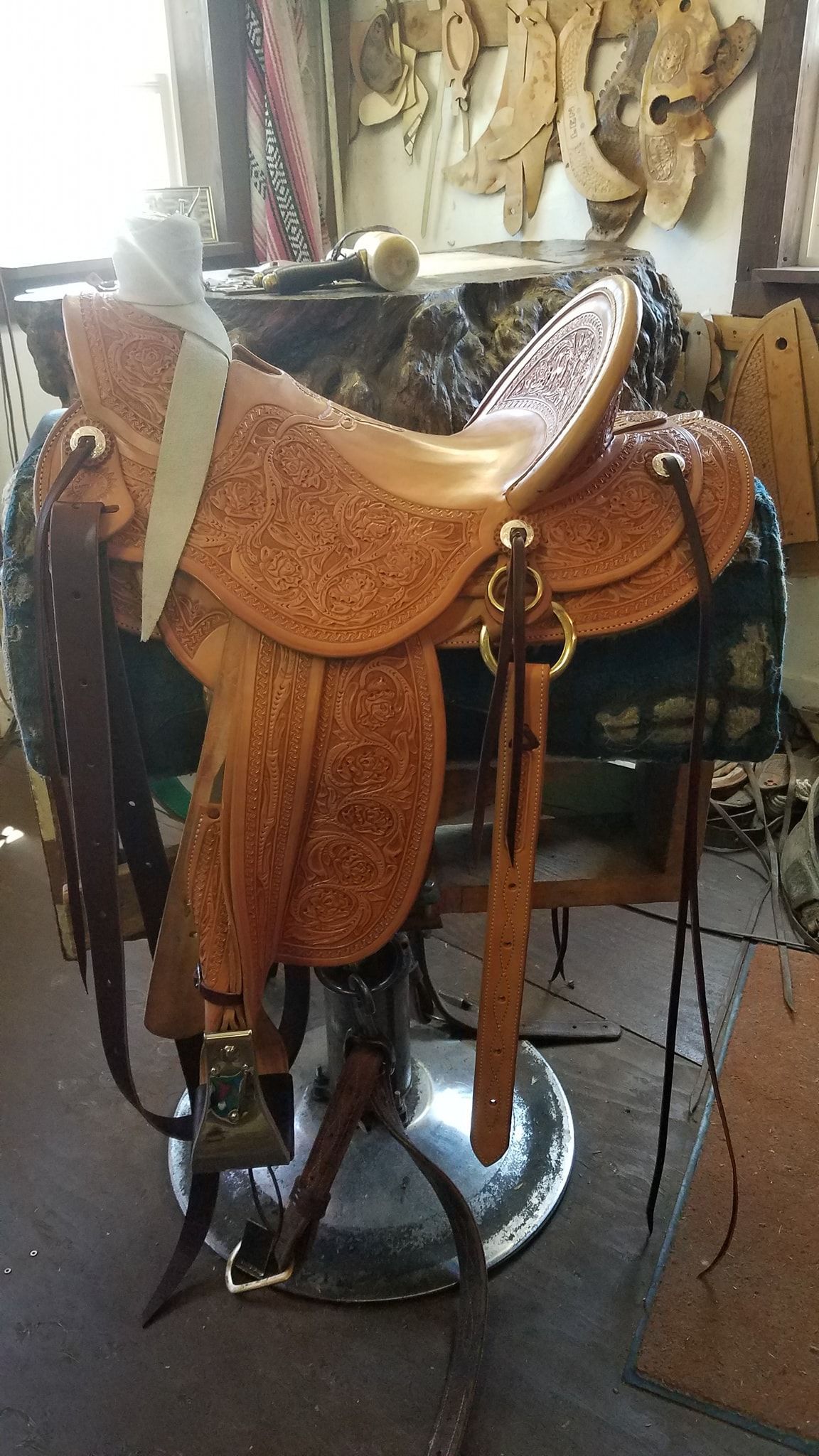 Brown western saddle on a metal stand indoors, with decorative leather tooling and stirrups attached