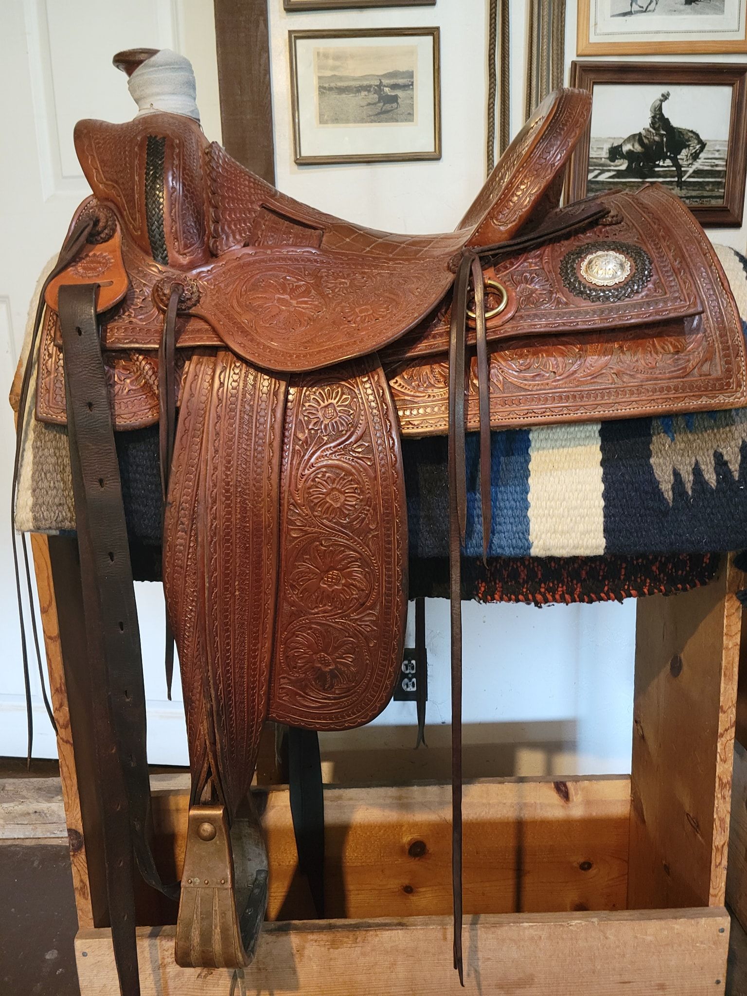 Brown leather horse saddle displayed on a wooden stand indoors