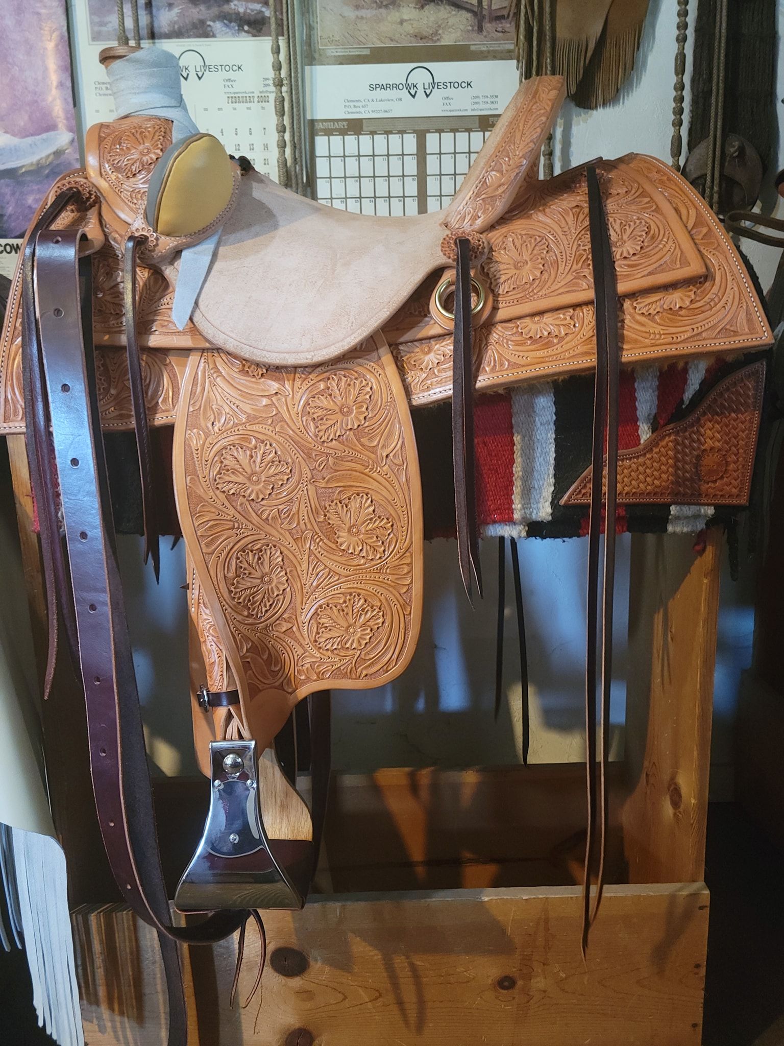 Rustic leather saddle and harness gear displayed on a wooden stand in a workshop.