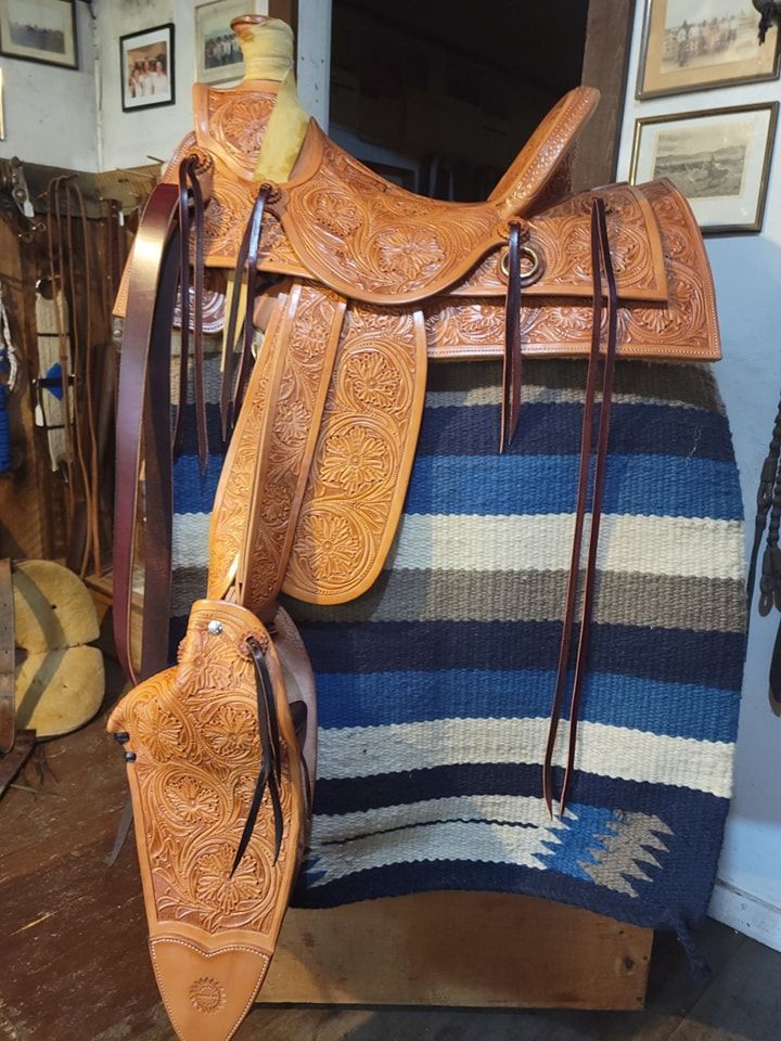 Orange leather saddle and bridle displayed on a striped blanket in a rustic room