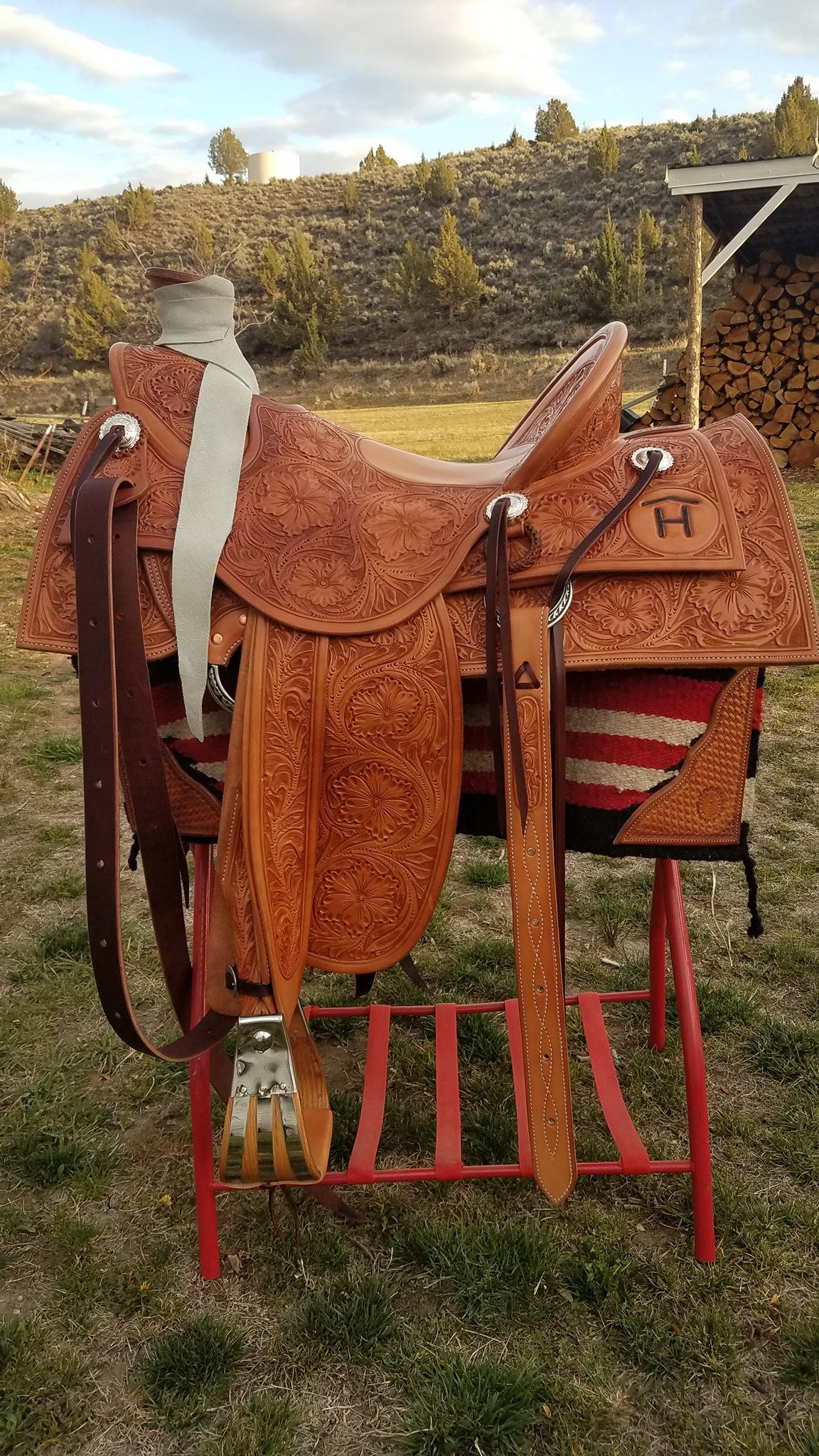Rust-colored outdoor chair draped with a patterned blanket, sitting on grass in a yard