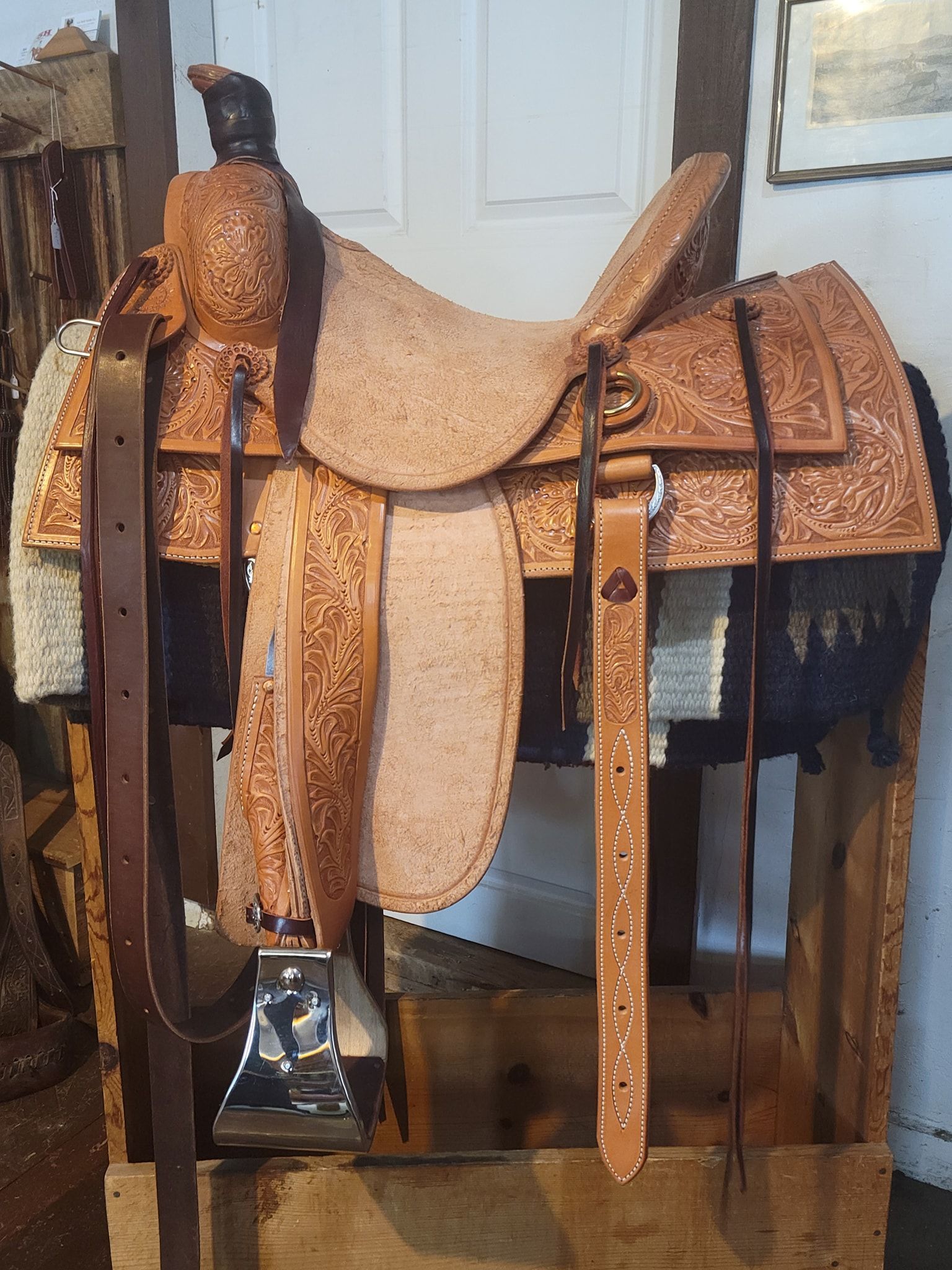 Leather saddle on a stand with tan seat and brown straps in front of a white door