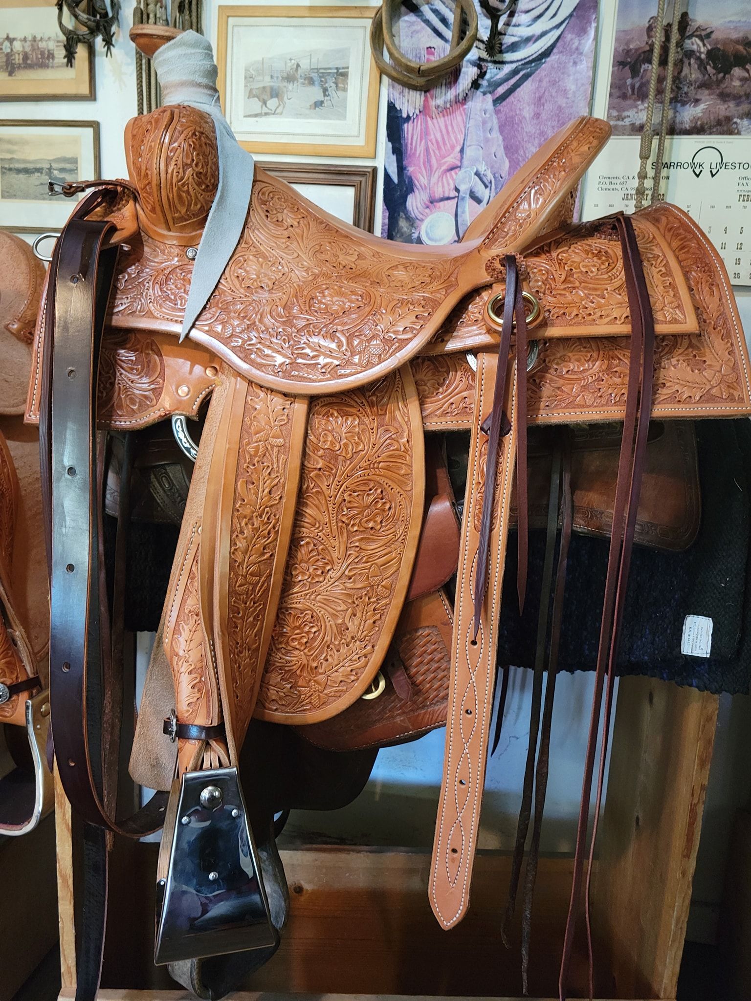 Brown leather saddle with stirrups hanging in a workshop or tack room