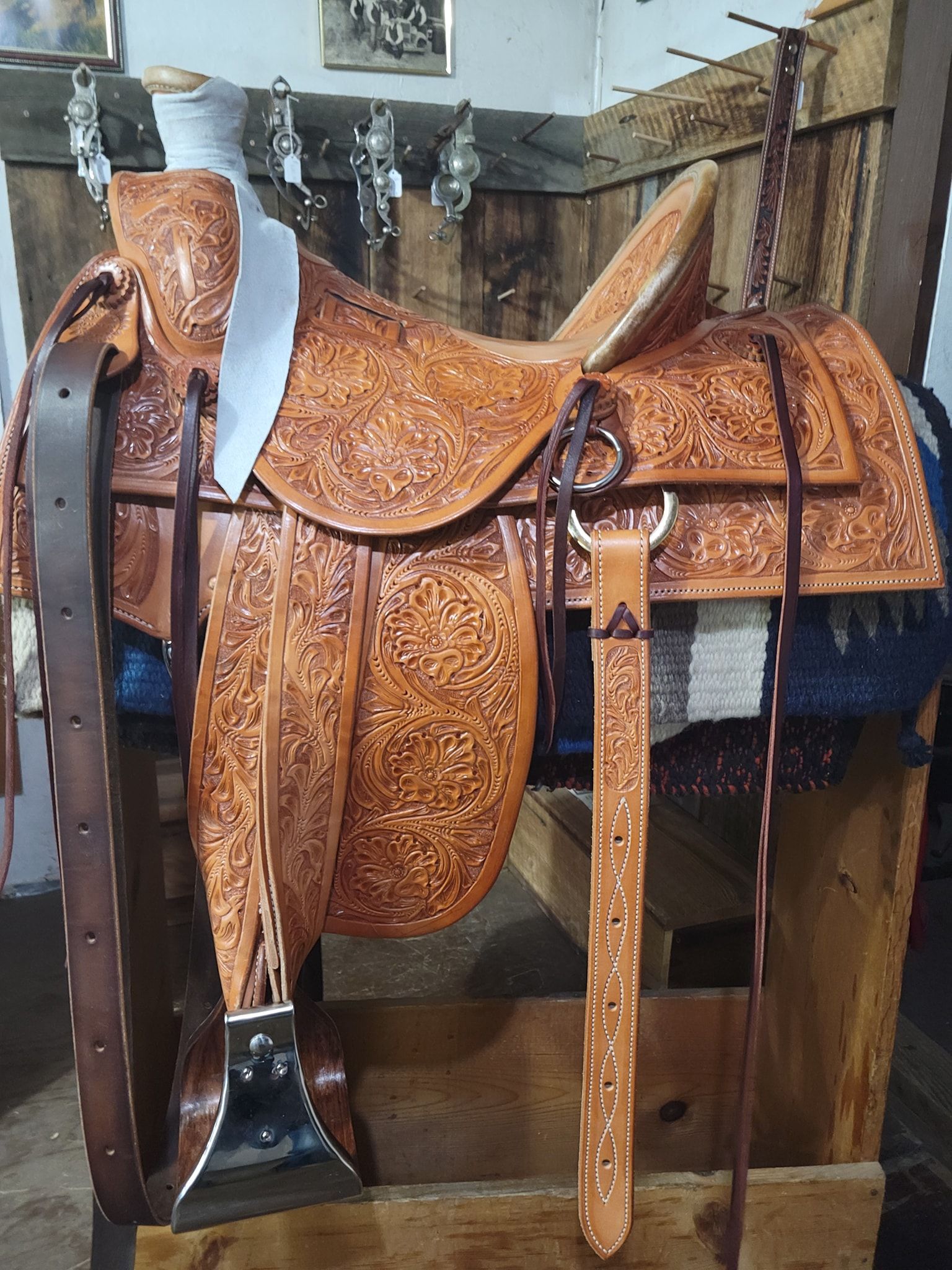 Leather saddle with carved brown tooled design displayed on a stand indoors