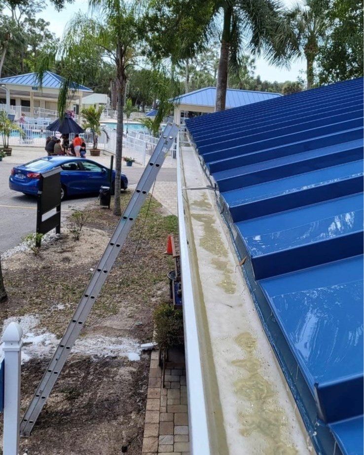 An aluminum extension ladder leans against a building's white gutter along a blue metal roof at a resort.