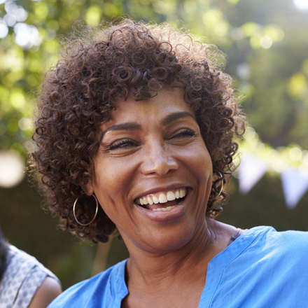 Smiling person in a blue shirt outdoors with blurred greenery in the background