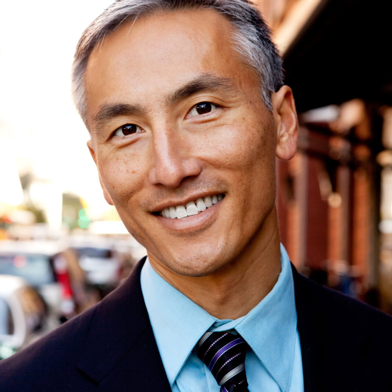 Smiling person in a blue shirt and striped tie outdoors on a city street