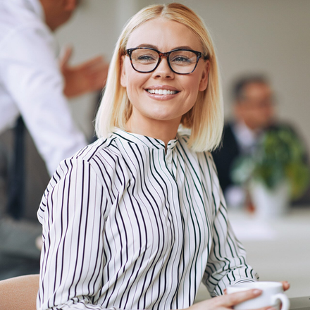 Smiling woman with glasses holding a cup in a bright office setting