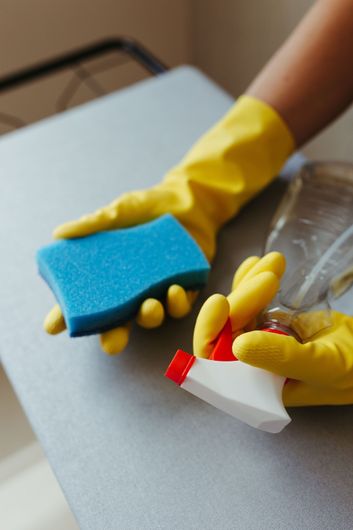 Gloved hands cleaning a surface with sponge and spray bottle on a table