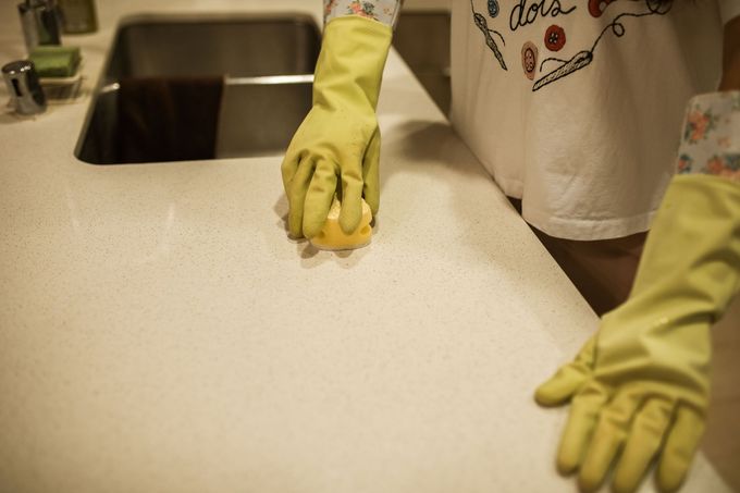 Gloved hand cleaning a gold faucet beside a white sink and mirror