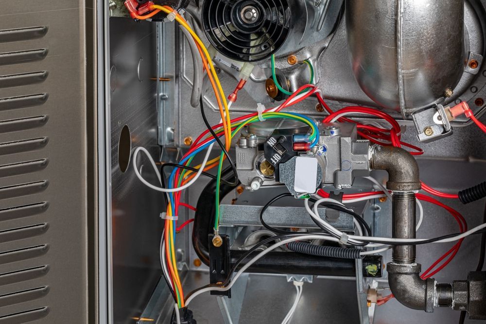 Inside of a furnace, showing wires, a fan, gas valve, and other components.