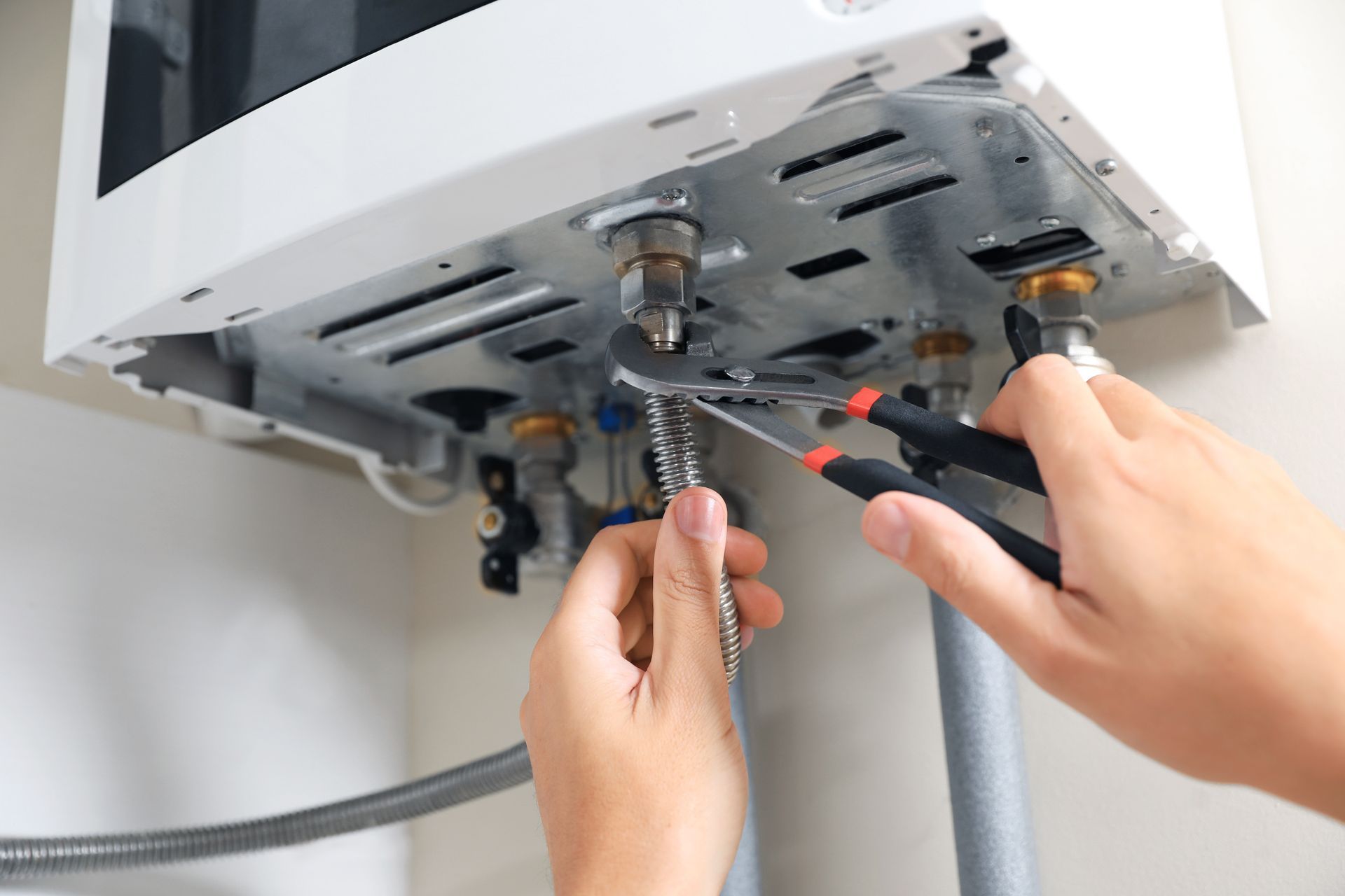 Hands using pliers and wrench to repair a white wall-mounted water heater.