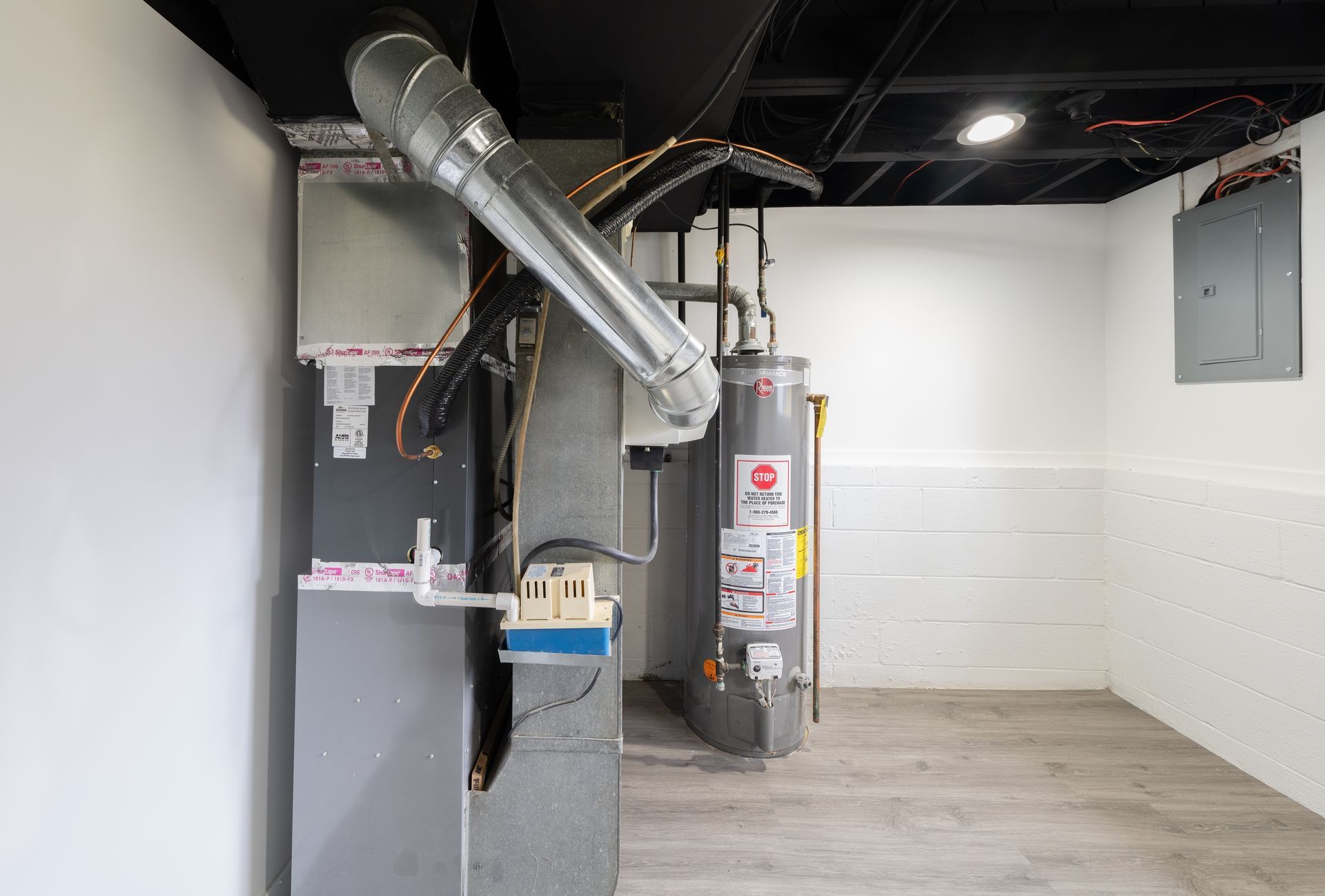 Basement with HVAC system, water heater, ductwork, and electrical panel against white walls and ceiling.