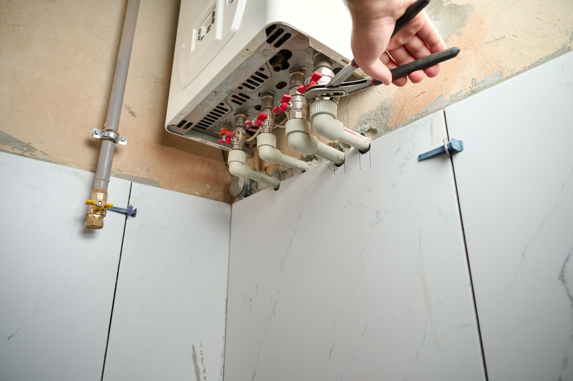 A person using a wrench to work on a white gas water heater mounted on a wall.