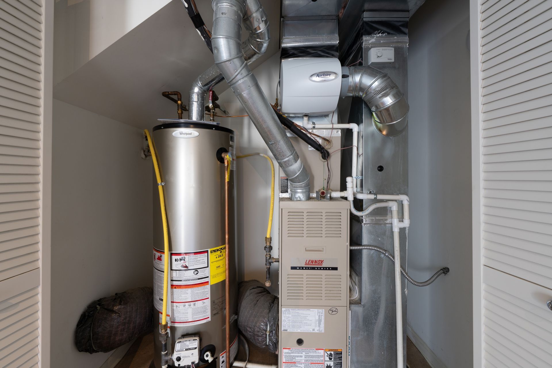Water heater and furnace in a utility closet with vent pipes and ductwork.