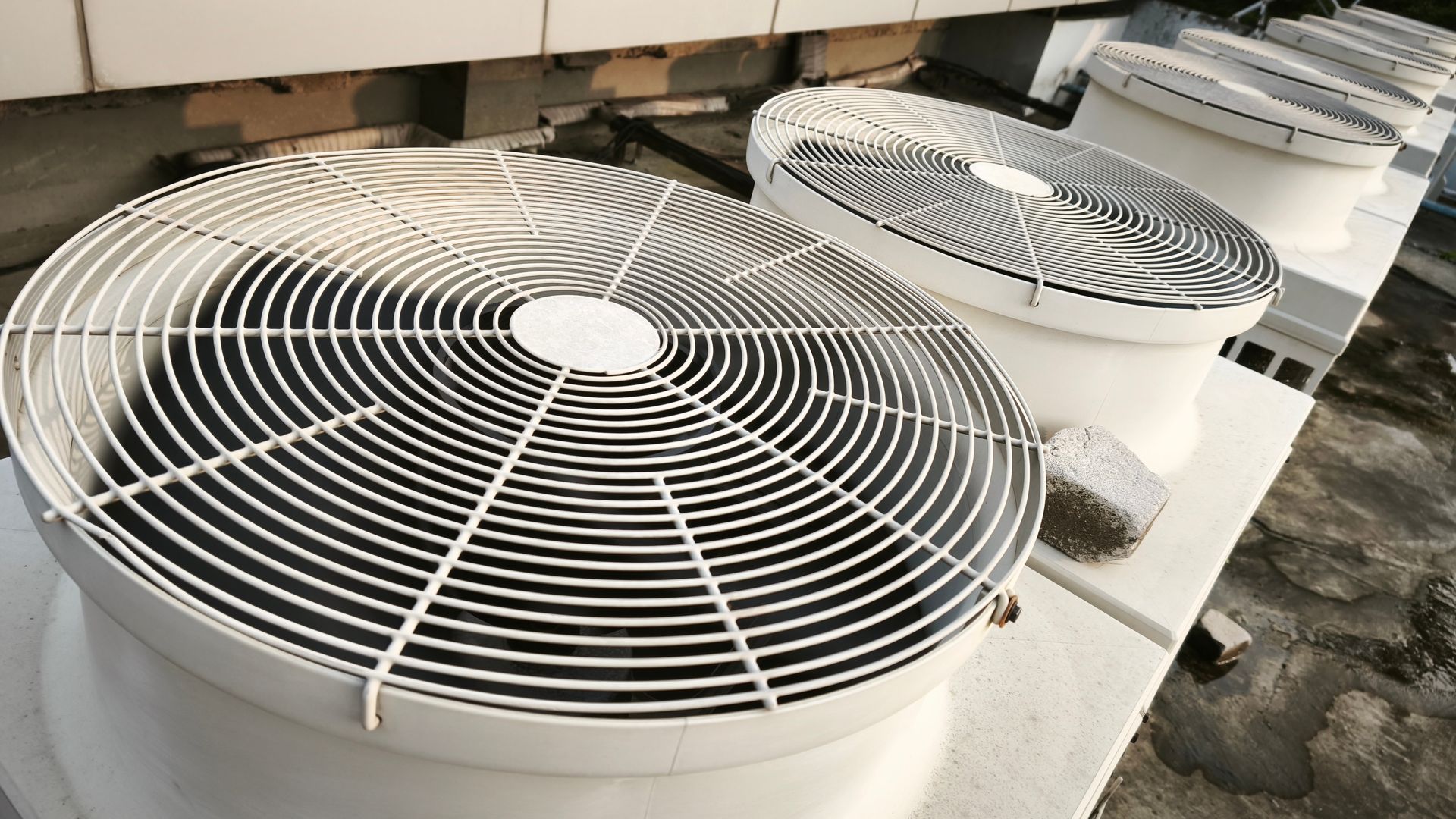 Row of rooftop air conditioning units with large, circular fans.
