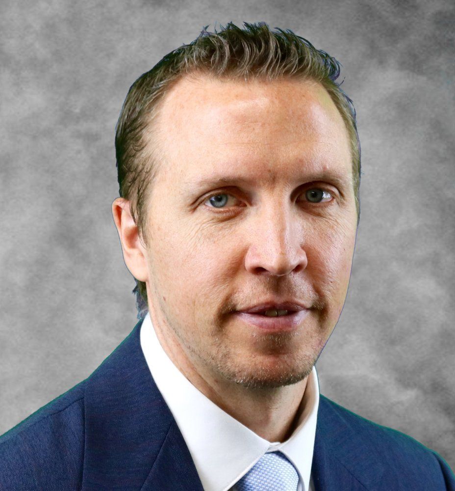 matthew sauer in a suit and tie is looking at the camera