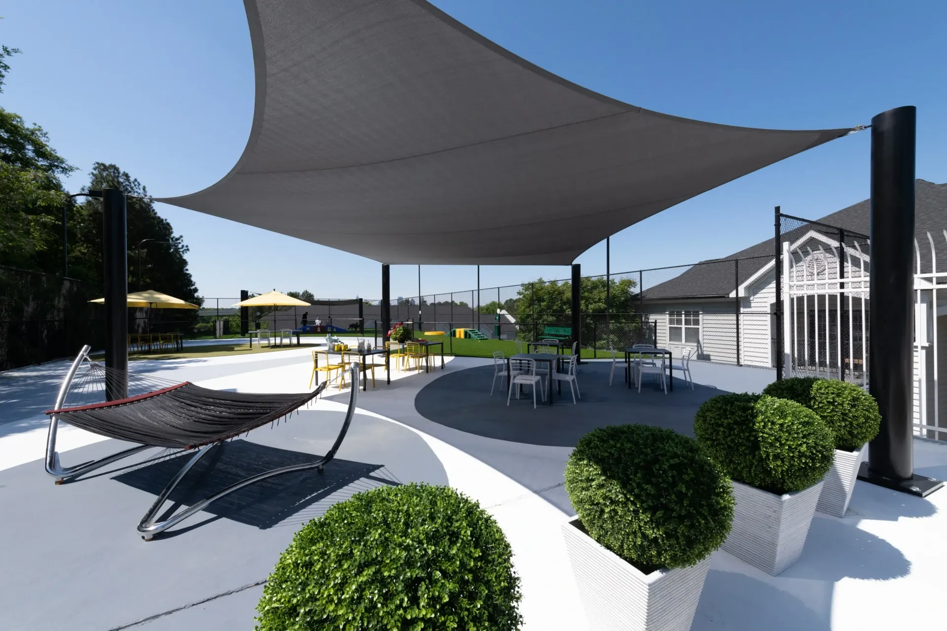 Outdoor lounge area with a hammock, shaded seating, and tennis courts in the background.