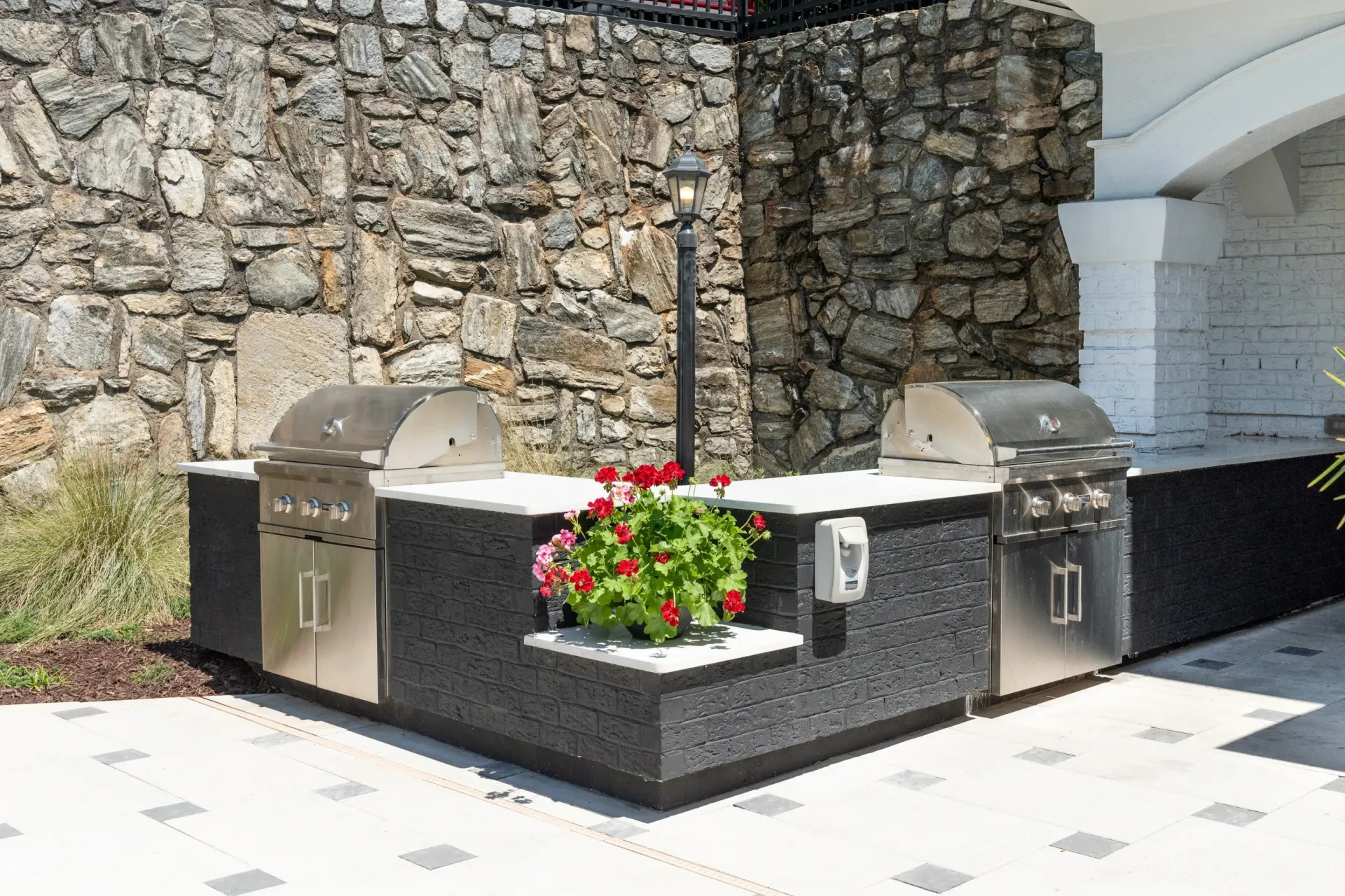 Outdoor grilling station with two stainless steel grills and a stone wall backdrop.